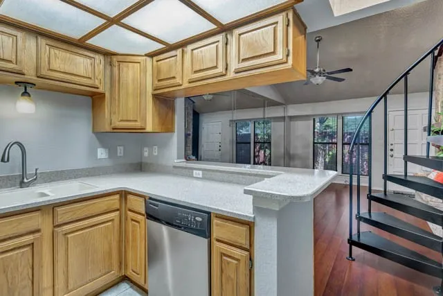 Kitchen featuring wood cabinetry, stone-finish countertops, stainless steel dishwasher, coffered lighting, and a black metal spiral staircase