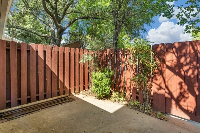 Private outdoor area featuring a concrete patio, wood-slat perimeter fencing, and mature trees