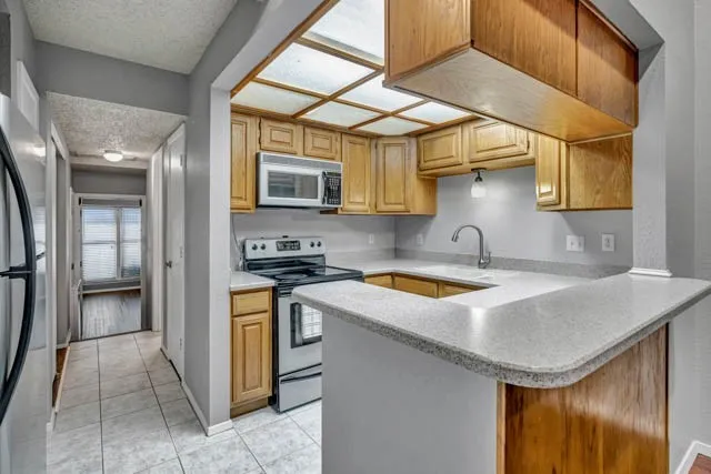 Kitchen featuring wood cabinetry, stone-finish countertops, stainless steel appliances, a tile floor, and an integrated ceiling light grid