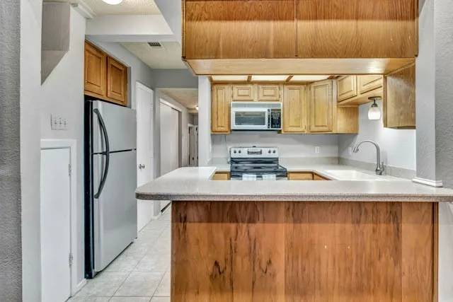 Kitchen featuring wood cabinetry, a peninsula countertop, stainless steel refrigerator, built-in microwave, and tile flooring