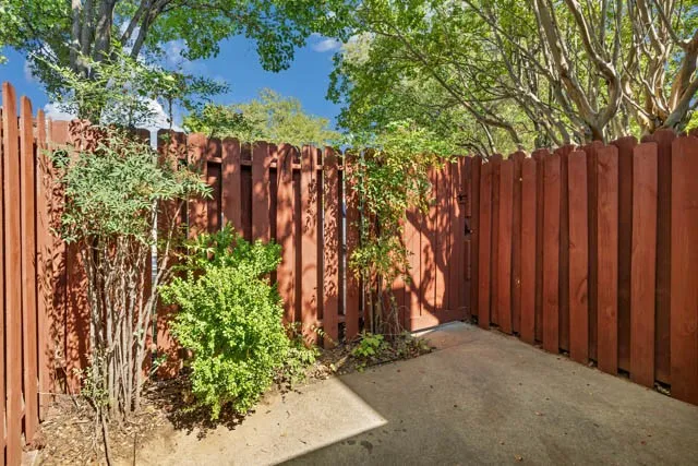 Concrete patio area enclosed by a solid wood privacy fence with mature tree canopy and established landscaping