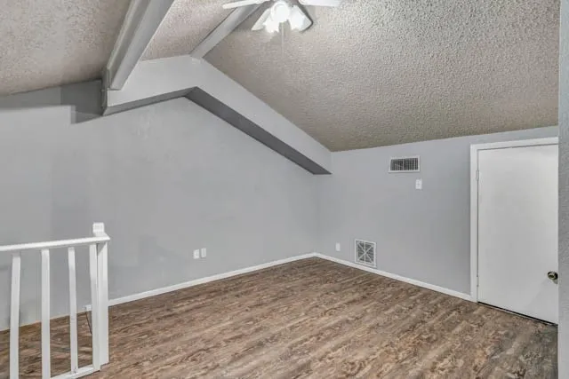 Vaulted ceiling with exposed beam, wood-finish flooring, and white railing