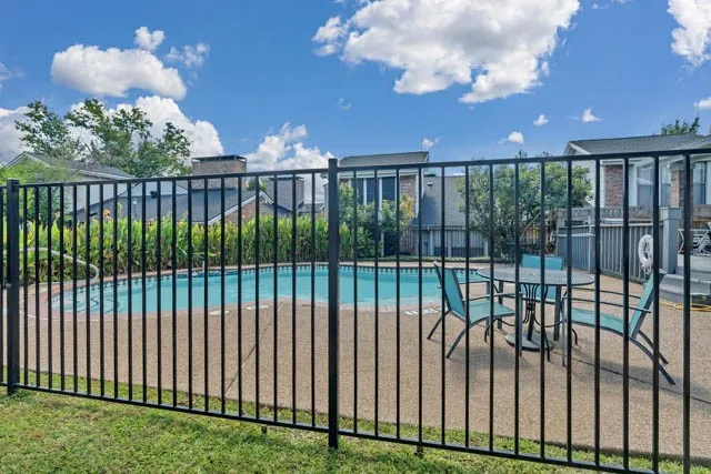 In-ground swimming pool with a concrete surround, enclosed by a black metal perimeter fence
