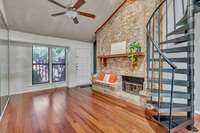 Vaulted ceiling, wood-finish flooring, floor-to-ceiling brick fireplace with a wood mantel, and a metal spiral staircase