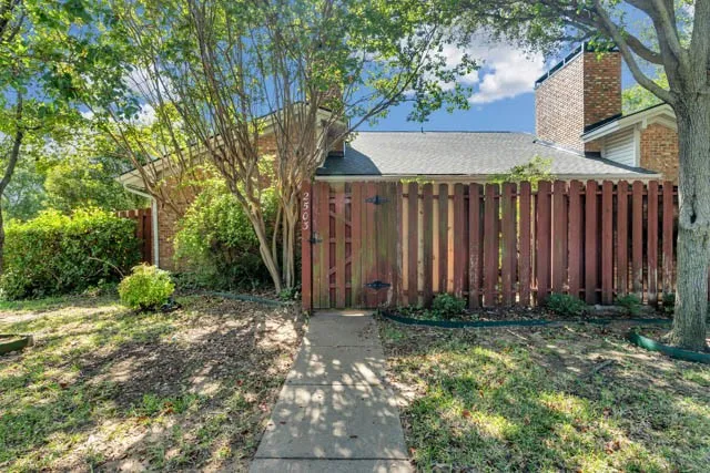 Brick exterior with a prominent chimney, concrete walkway, and wood privacy fencing