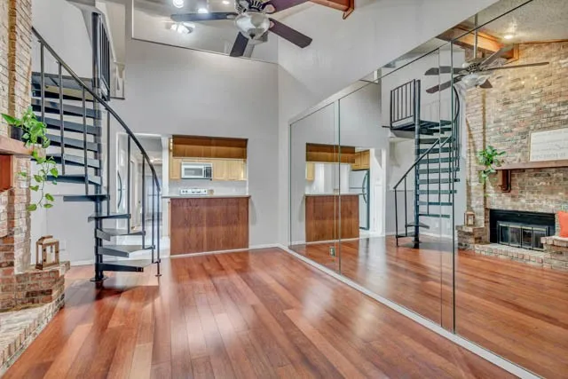 Vaulted ceiling featuring a metal spiral staircase, wood-finish flooring, floor-to-ceiling mirror wall, and a floor-to-ceiling brick fireplace