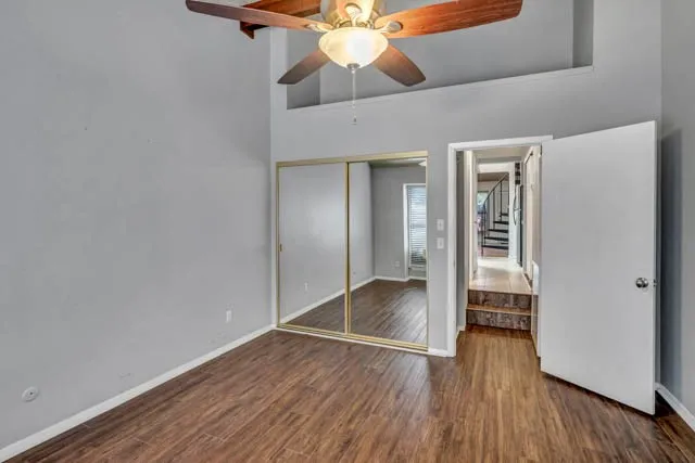High-ceiling interior featuring wood-finish flooring, a ceiling fan with integrated lighting, and a dual-panel mirrored closet