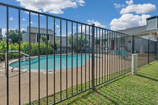 In-ground pool with aggregate pool decking, enclosed by a black metal security fence, set against a manicured lawn