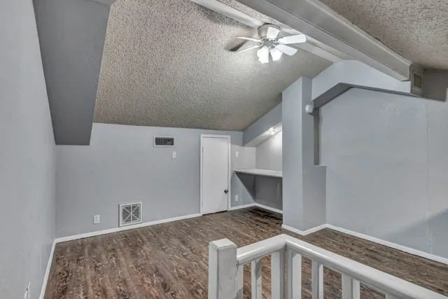 Vaulted ceiling featuring a central lighted ceiling fan, wood-finish flooring, built-in desk area, and painted solid-core door