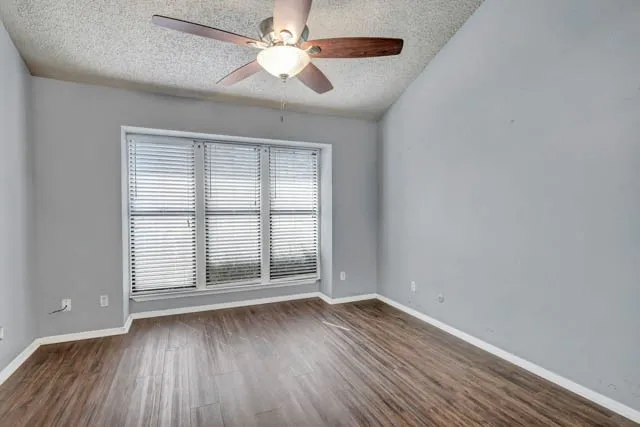 Vaulted ceiling with integrated ceiling fan, wood-finish flooring, and a large triple-pane window with horizontal blinds
