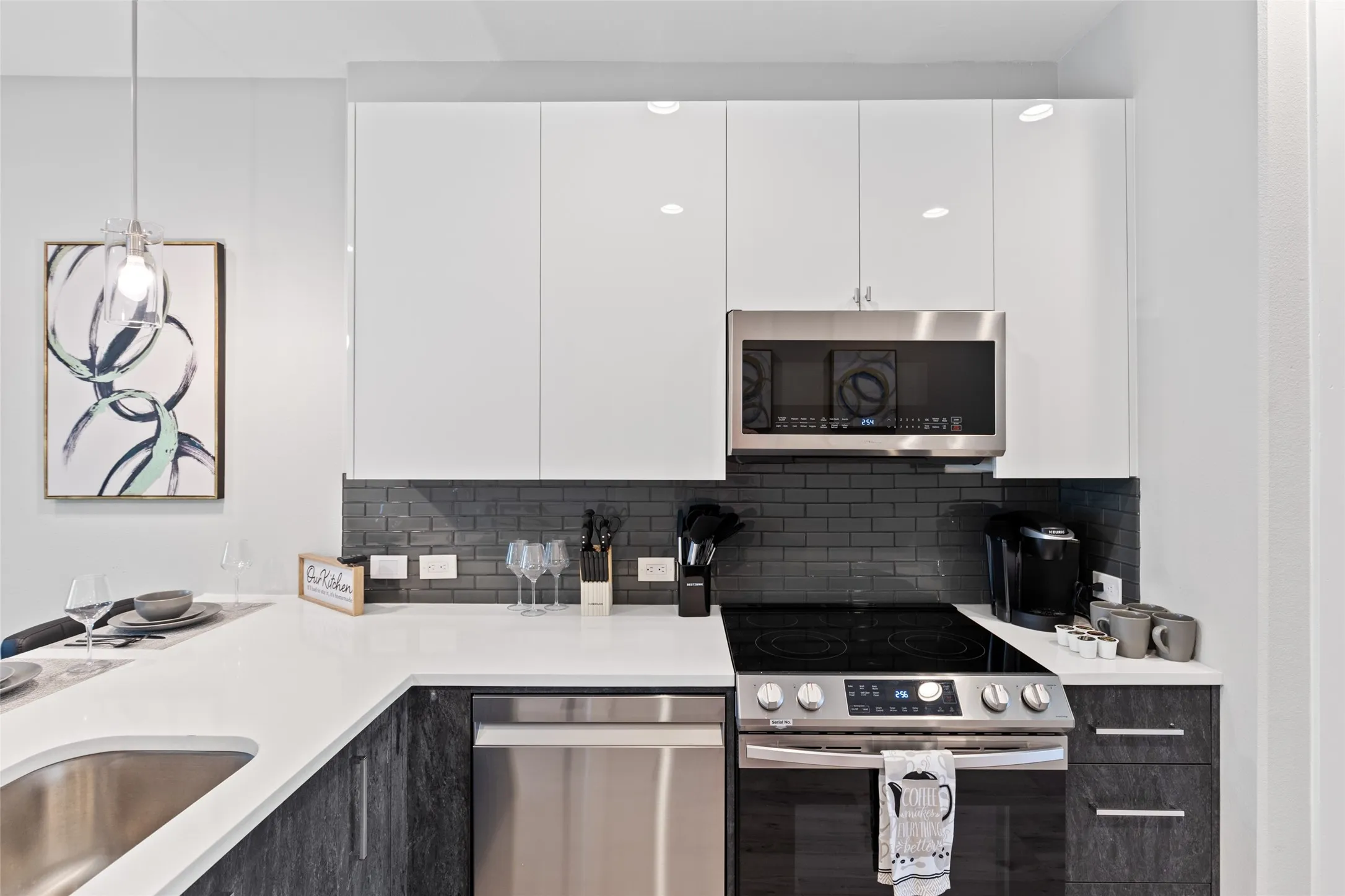 White flat-panel cabinetry, stainless steel appliances, dark subway tile backsplash, white countertops, and an undermount sink