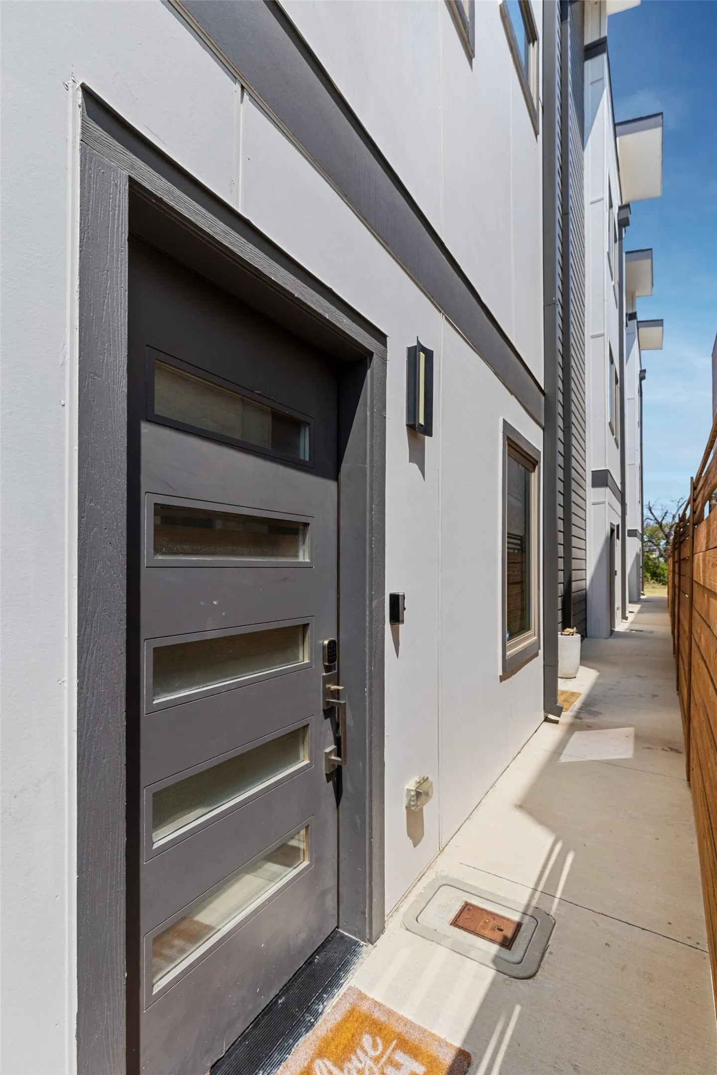 Contemporary exterior with clean lines, featuring a dark-framed entry door with multiple lites, a sleek exterior light fixture, and a concrete walkway