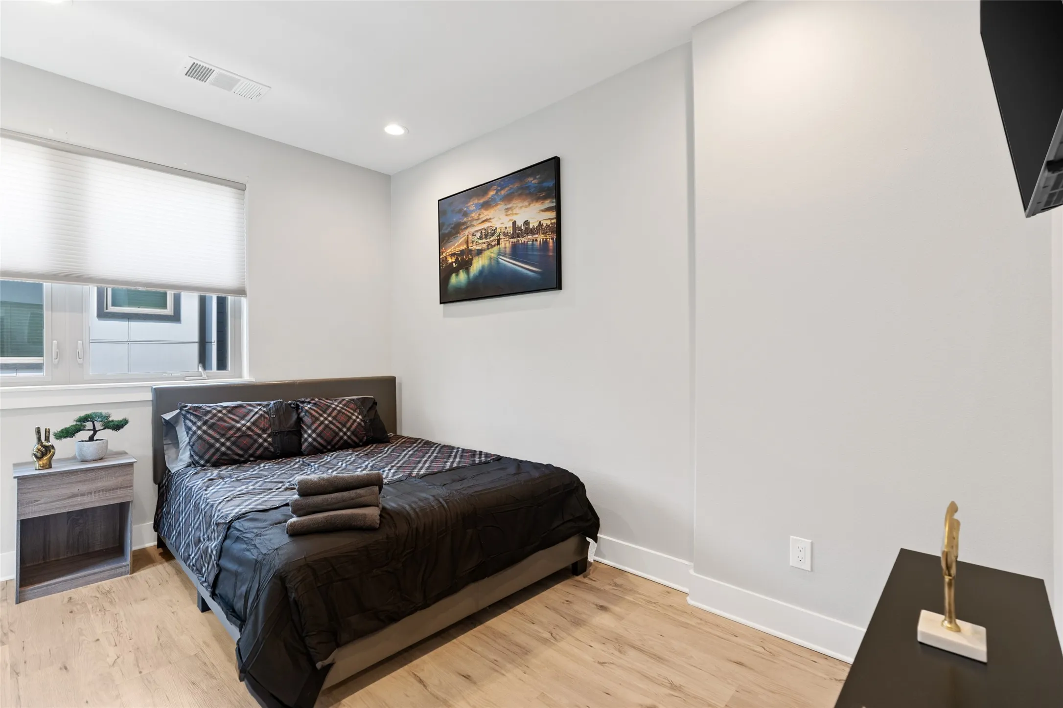 Light wood-finish flooring, recessed lighting, and a window with a pleated shade