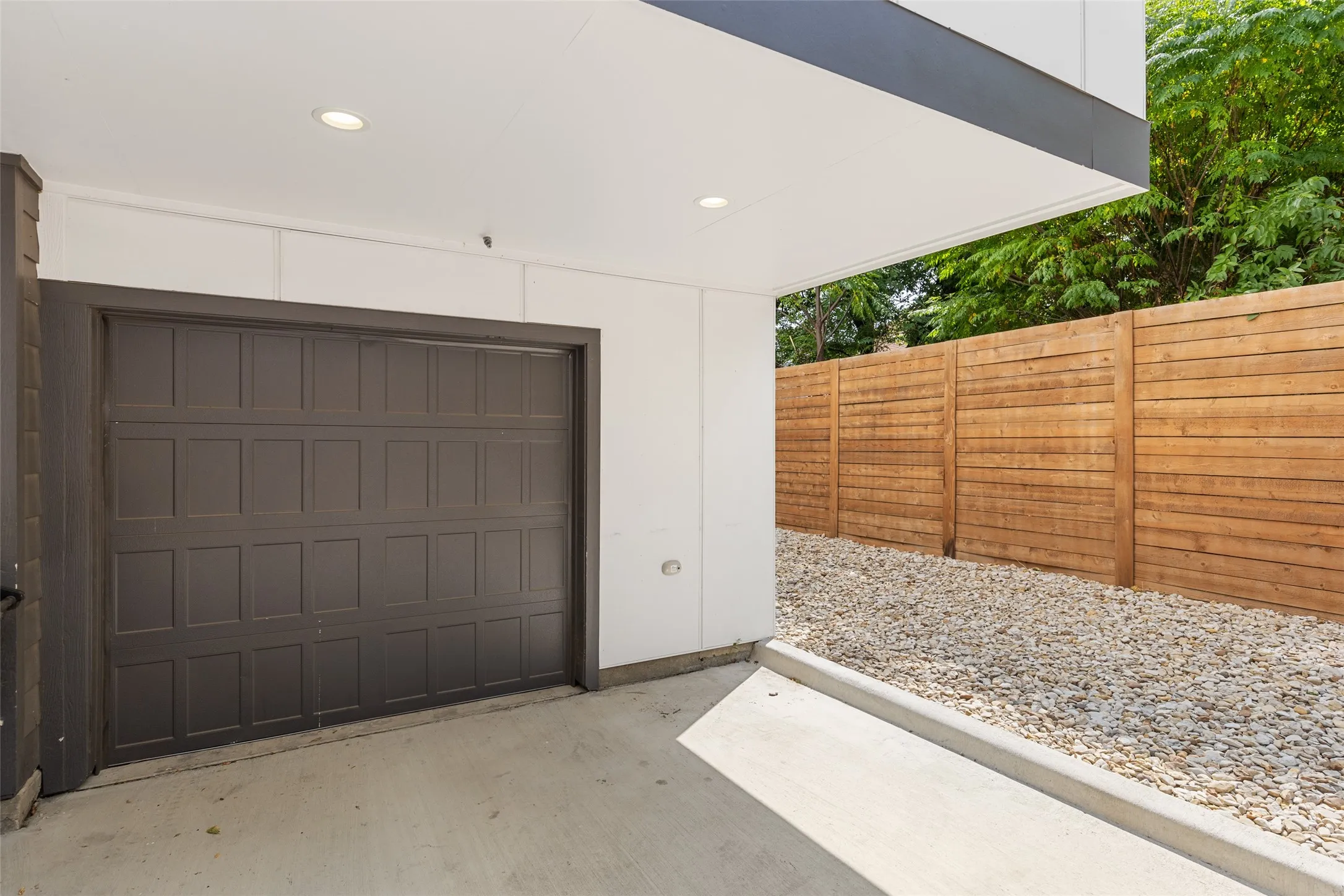 Attached garage with a panel-style door, concrete driveway, recessed lighting, and a wood privacy fence