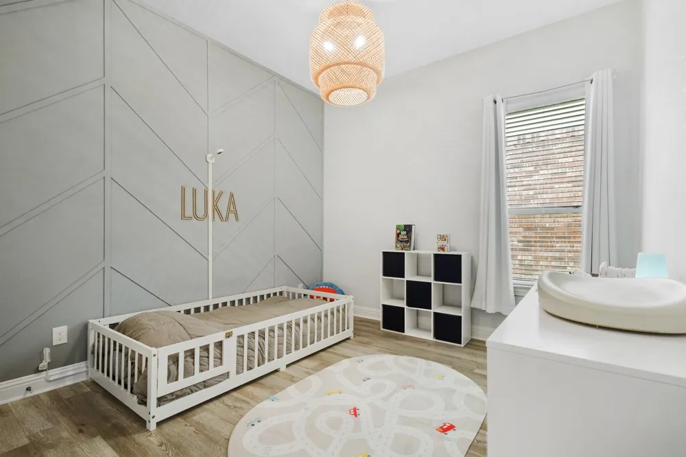 This secondary bedroom features an accent wall with geometric paneling, wood-finish flooring, and decorative lighting.