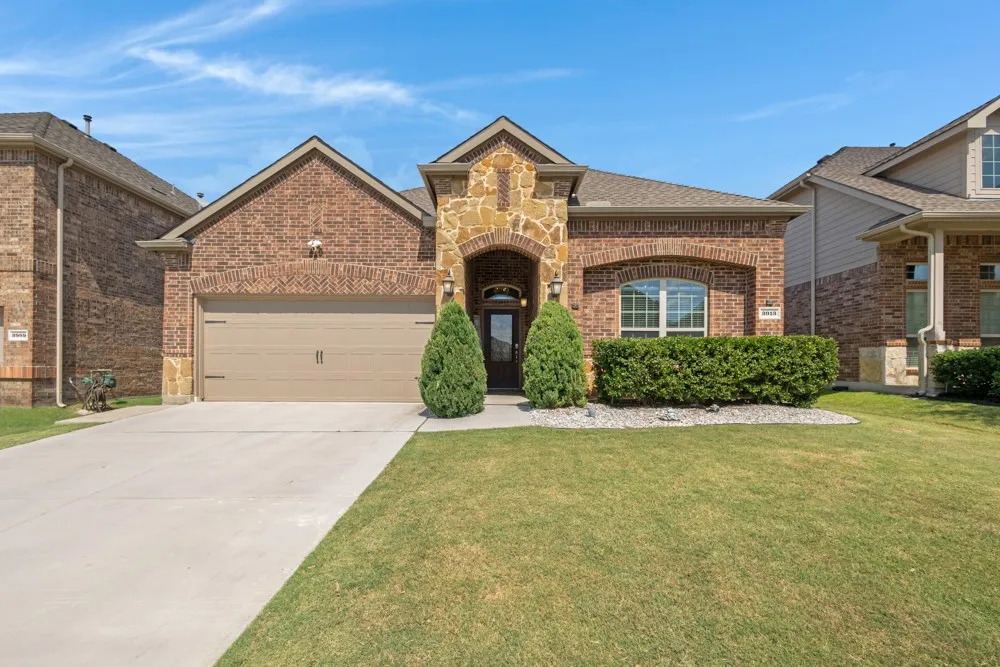 Brick and stone facade, arched entry, two-car garage, concrete driveway, and manicured landscaping