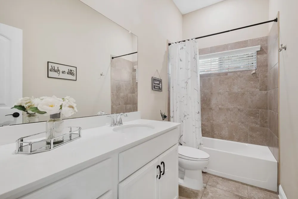 The guest bathroom centered between the 2 secondary bedrooms offers a white vanity with an integrated sink, polished chrome faucet, and expansive wall-mounted mirror.  Bath time for the kids will be a joy in this space!