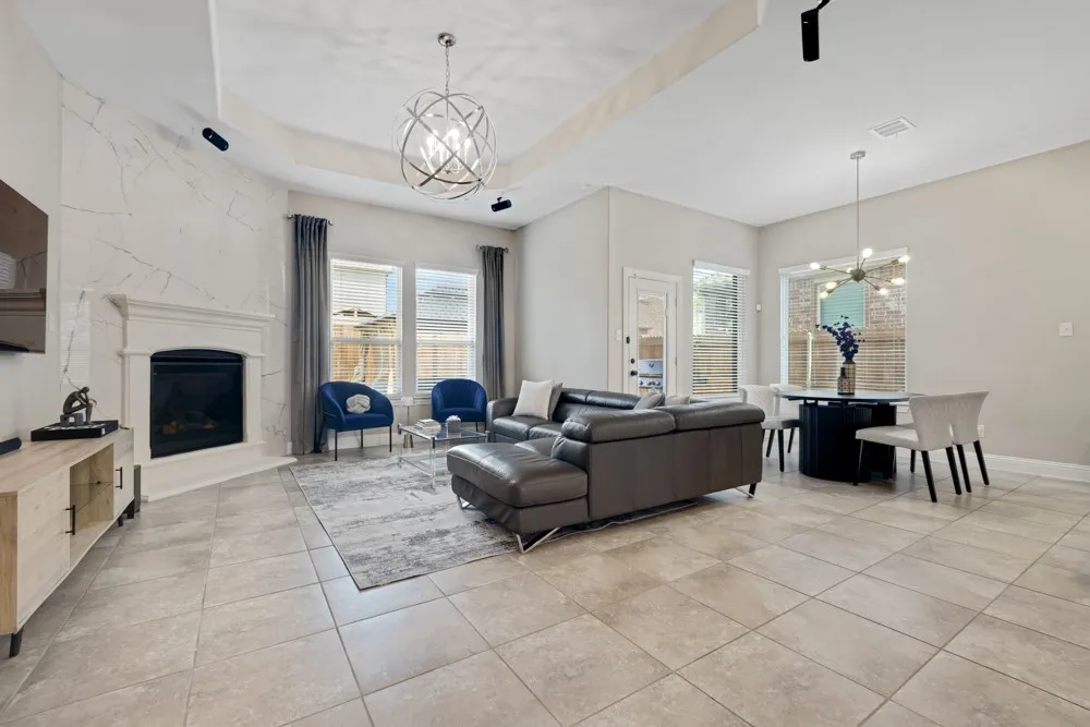 Spacious open-concept interior featuring light-toned tile flooring, a fireplace with a white mantel and floor to ceiling tile accent wall.