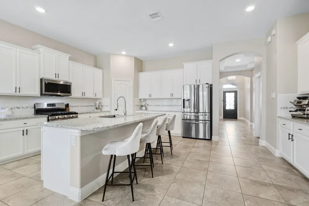 This spacious kitchen features white cabinetry, stainless steel appliances, granite counters, and a large center island that easily seats 4.