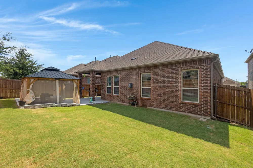 Expansive backyard featuring a manicured lawn, full brick exterior, a covered patio, and a screened in gazebo!