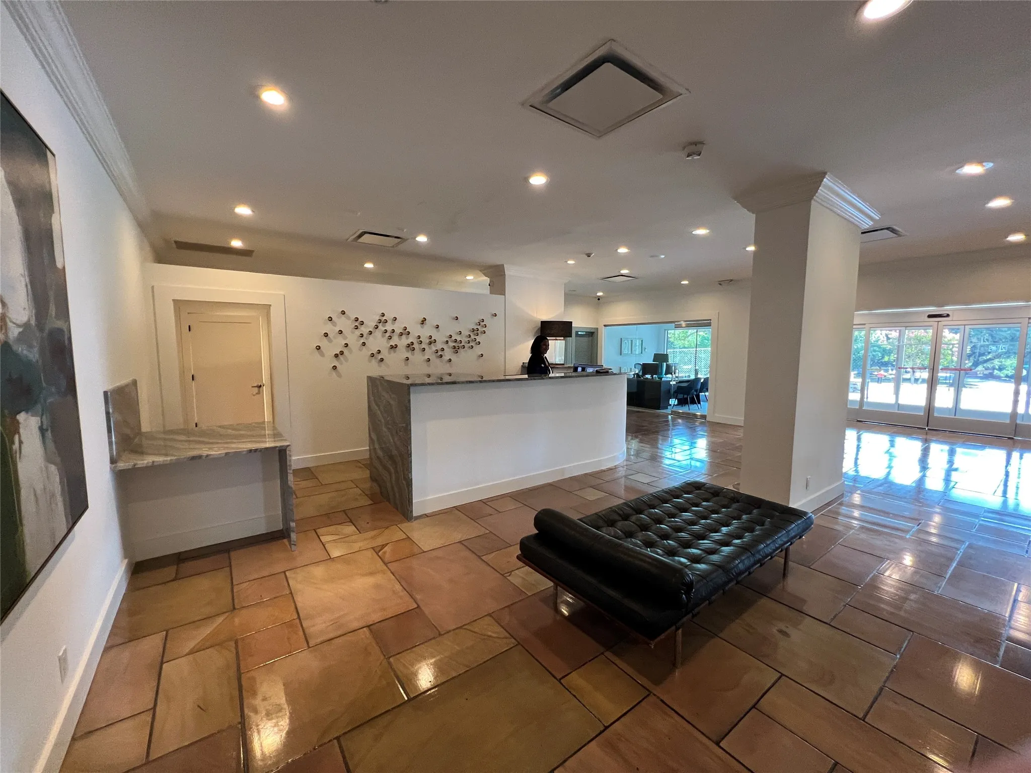 Irregular-cut stone flooring, built-in reception desk with a stone countertop, recessed lighting, crown molding, and expansive glass entry doors