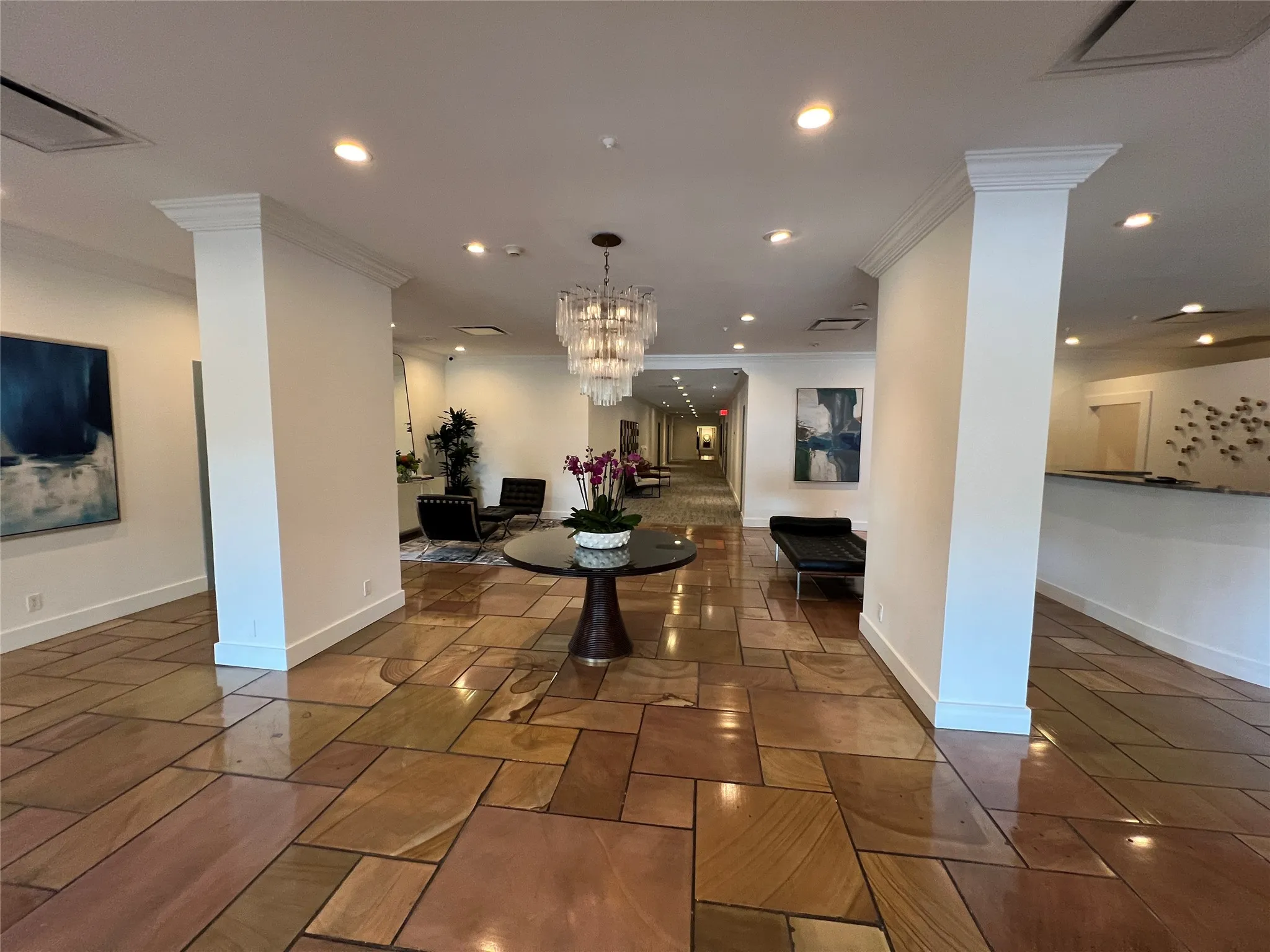 Spacious common area featuring varied stone flooring, recessed lighting, a tiered chandelier, and decorative columns