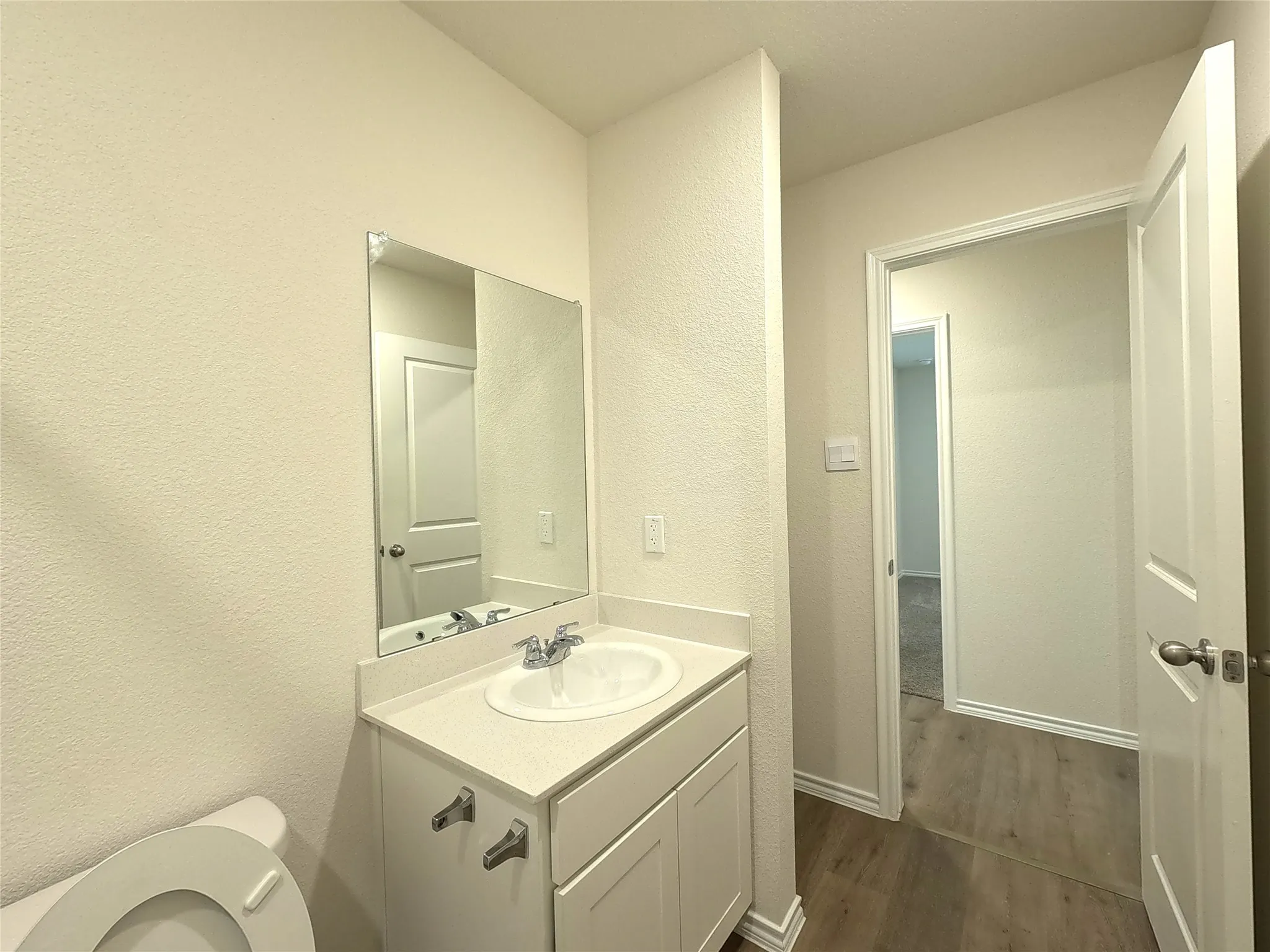 Vanity with an integrated sink and chrome faucet, large frameless mirror, and a wood-finish flooring