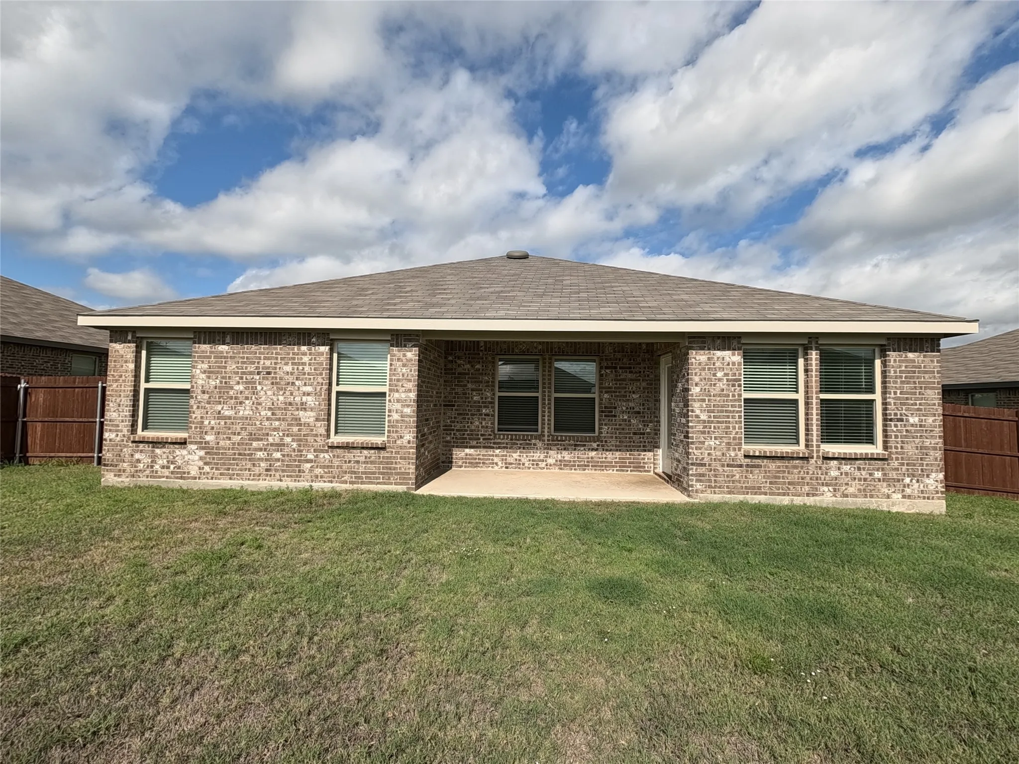 Rear exterior featuring a brick facade, covered patio, and multiple windows
