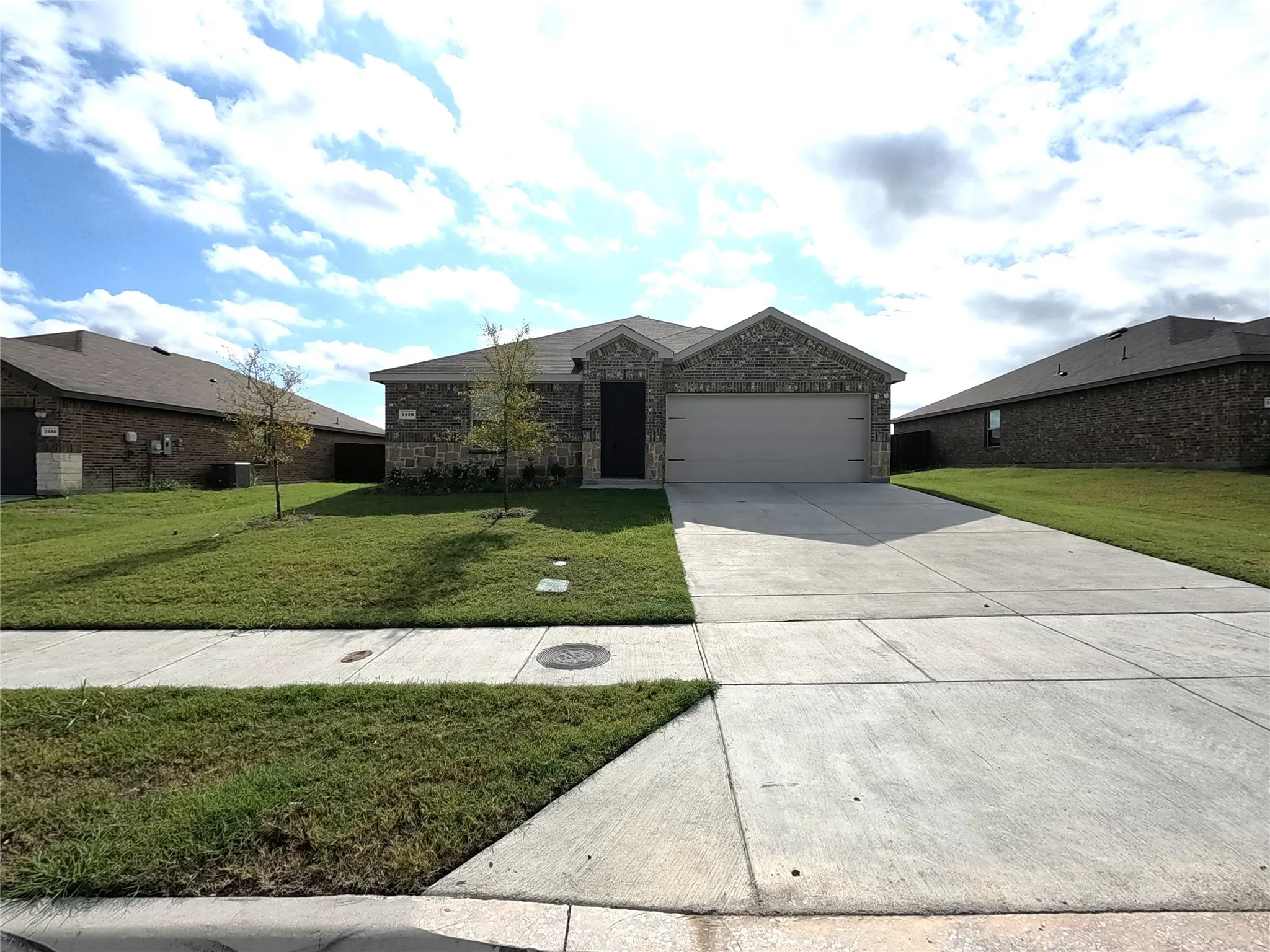 Brick facade, attached two-car garage, concrete driveway, and a front lawn