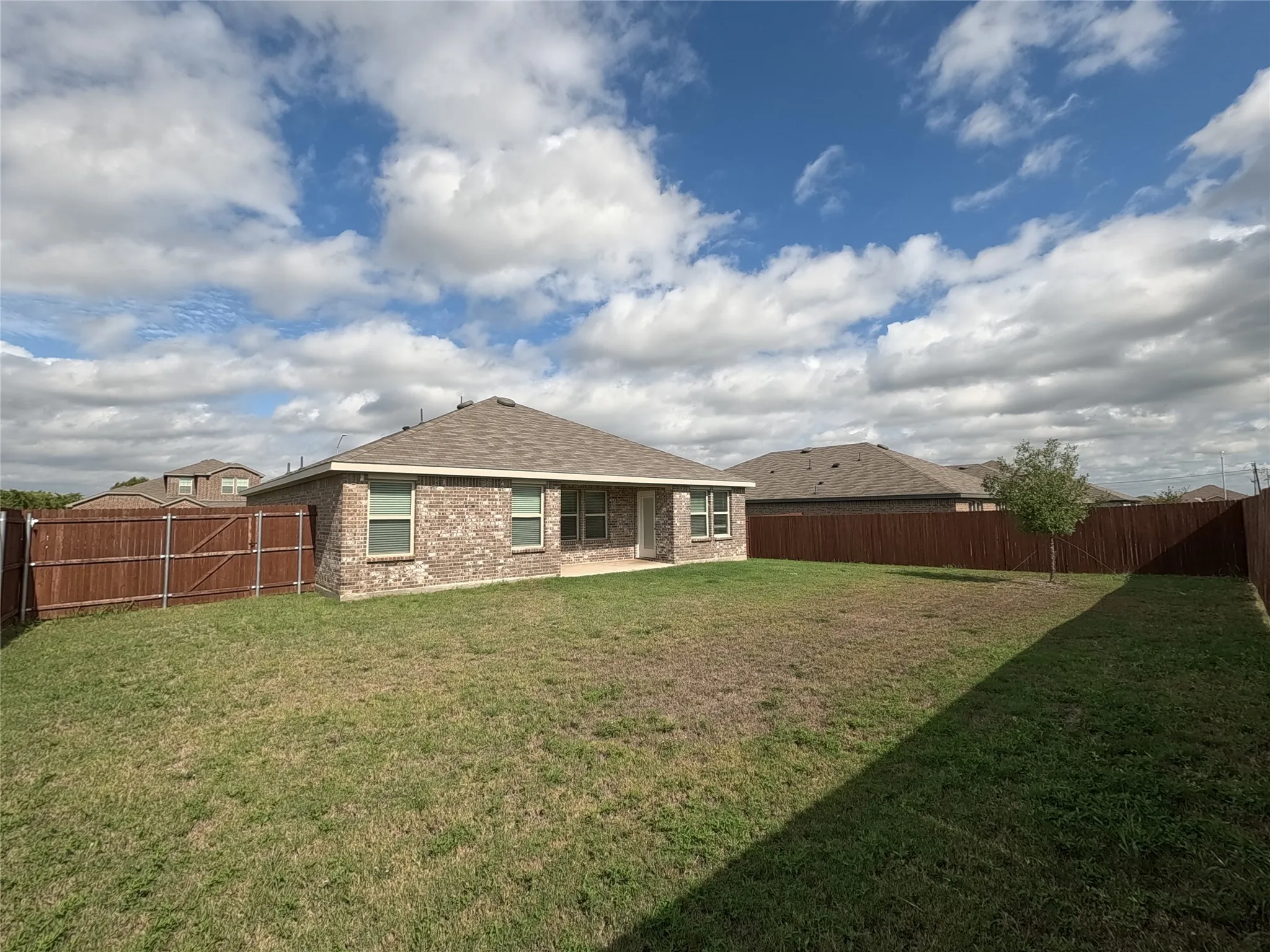 Expansive backyard featuring a manicured lawn, complete wood fencing, and a brick exterior home with a shingle roof