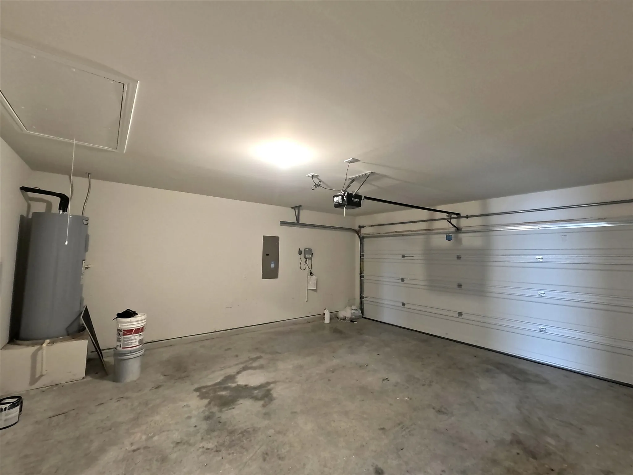 Garage with a roll-up door, exposed automatic garage door opener, and a water heater