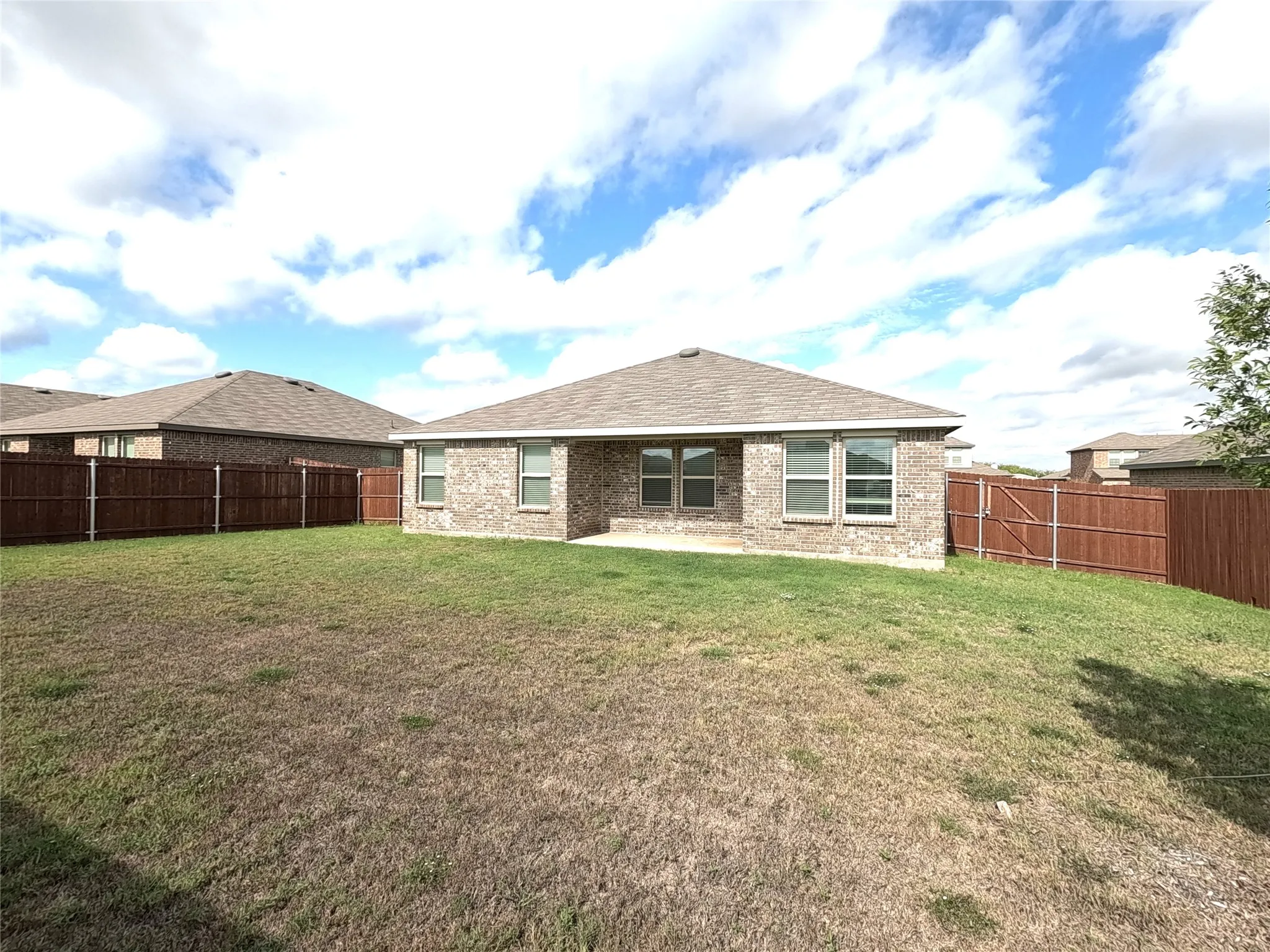 Brick exterior with a shingled roof, multiple windows, and a fully fenced backyard