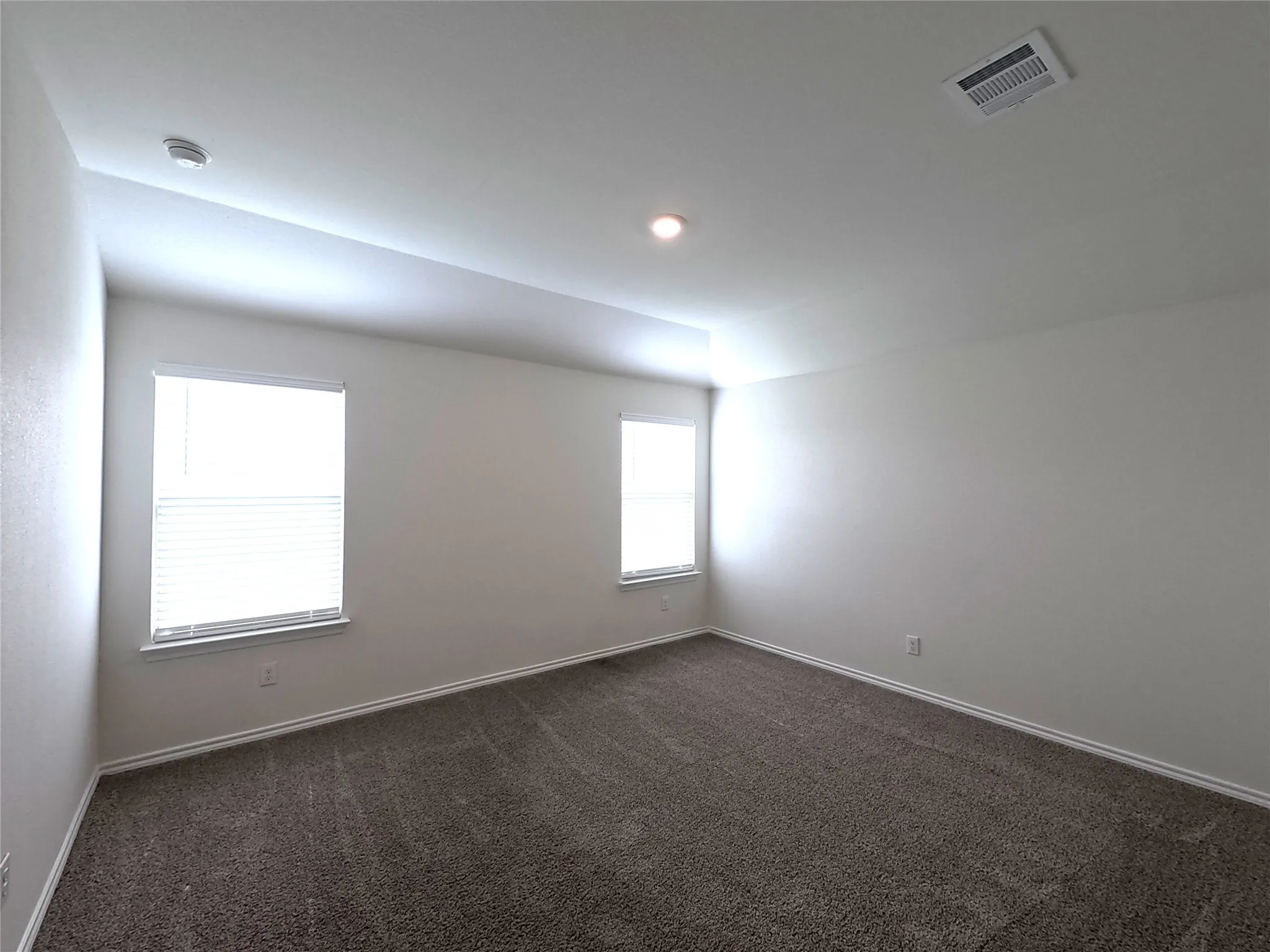 Spacious room with plush carpeting, multiple windows with blinds, recessed lighting, and a tray ceiling detail