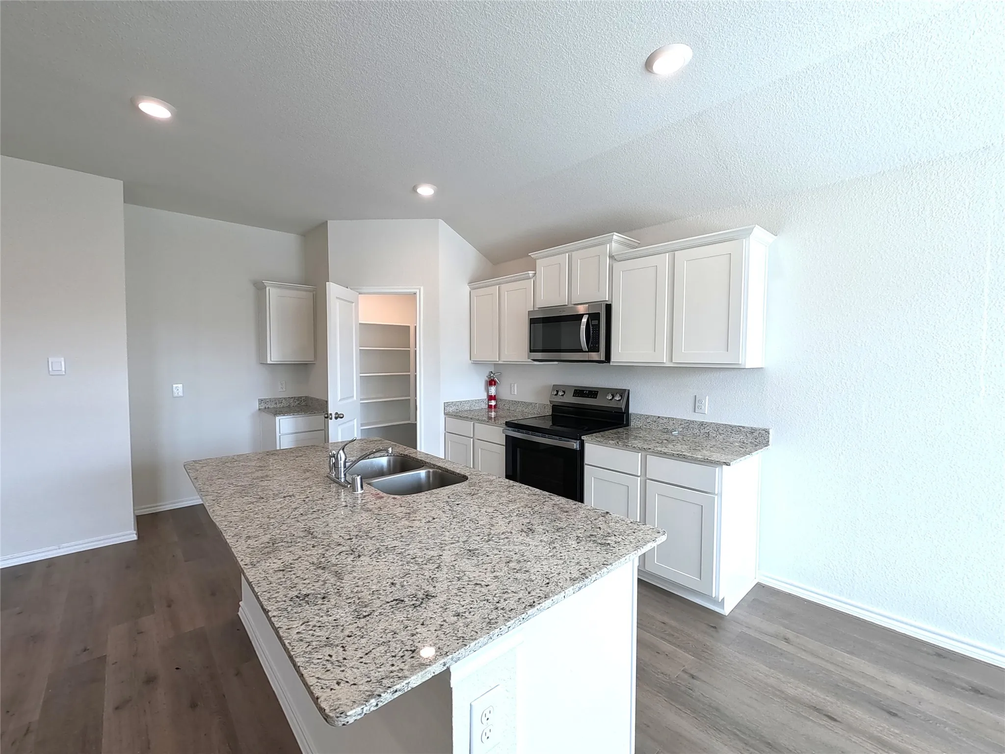 Kitchen featuring an island with dual basin sink, stainless steel appliances, granite countertops, white cabinetry, and wood-finish flooring