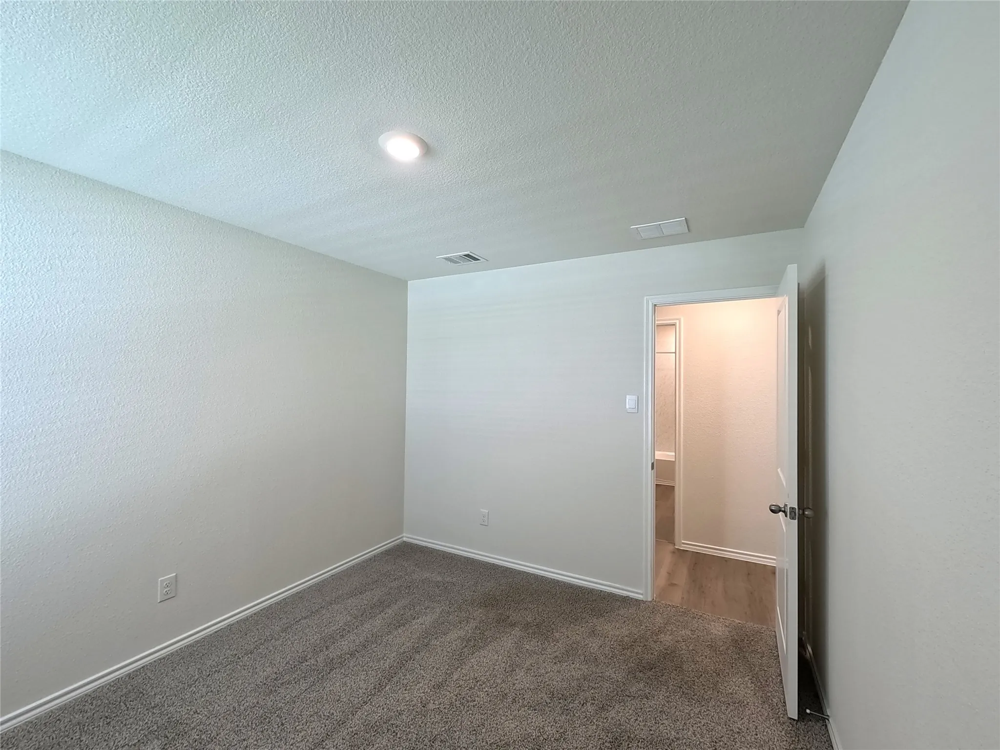 Recessed lighting, textured walls, gray carpeting, white trim, and a white interior door