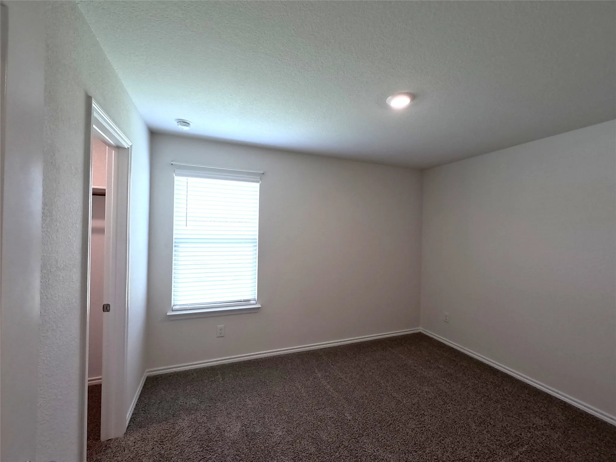 Recessed ceiling lighting, textured wall finish, window with horizontal blinds, neutral tone carpeting, and white trim