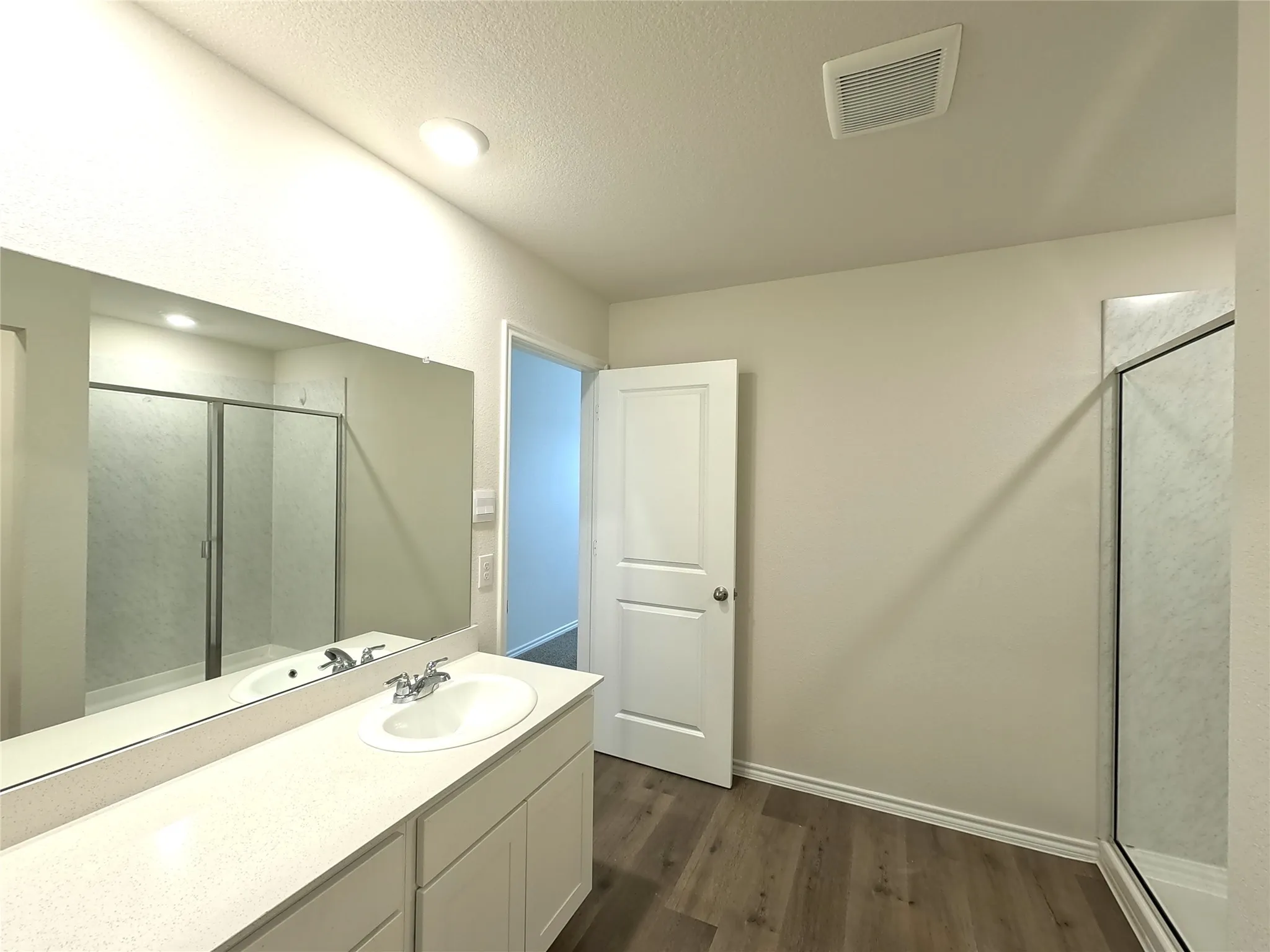 Vanity with a single basin sink, expansive mirror, wood-finish flooring, and a glass-enclosed shower
