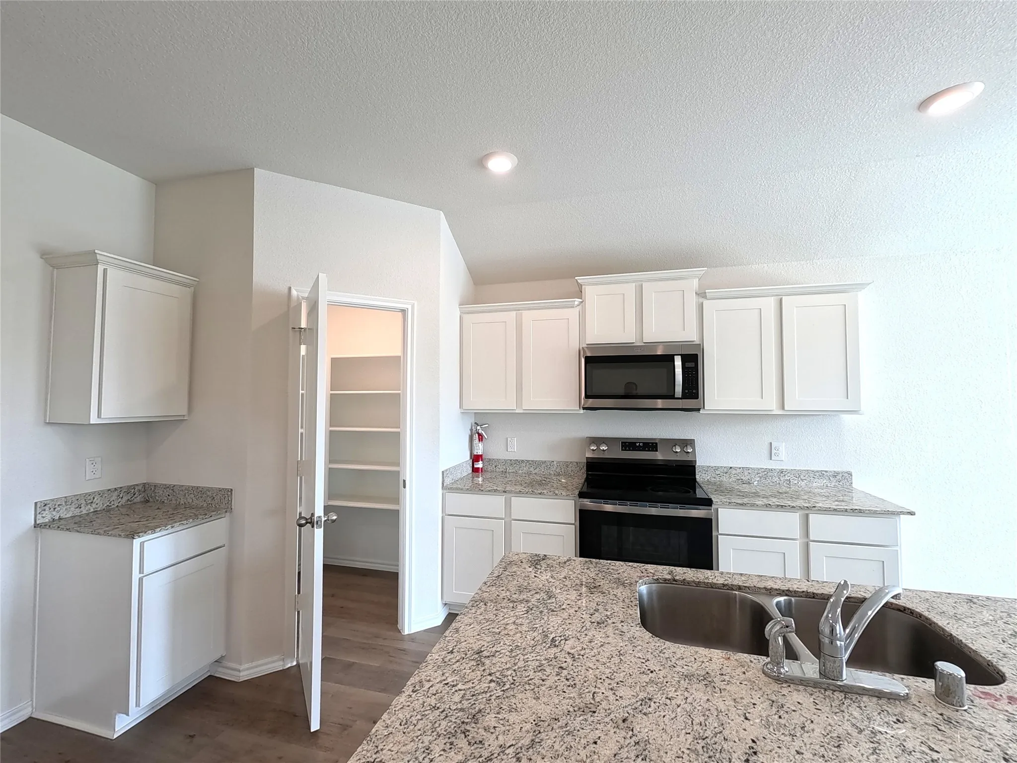 Kitchen featuring white cabinetry, granite-finish countertops, stainless steel microwave, black electric range, and a built-in pantry with shelving