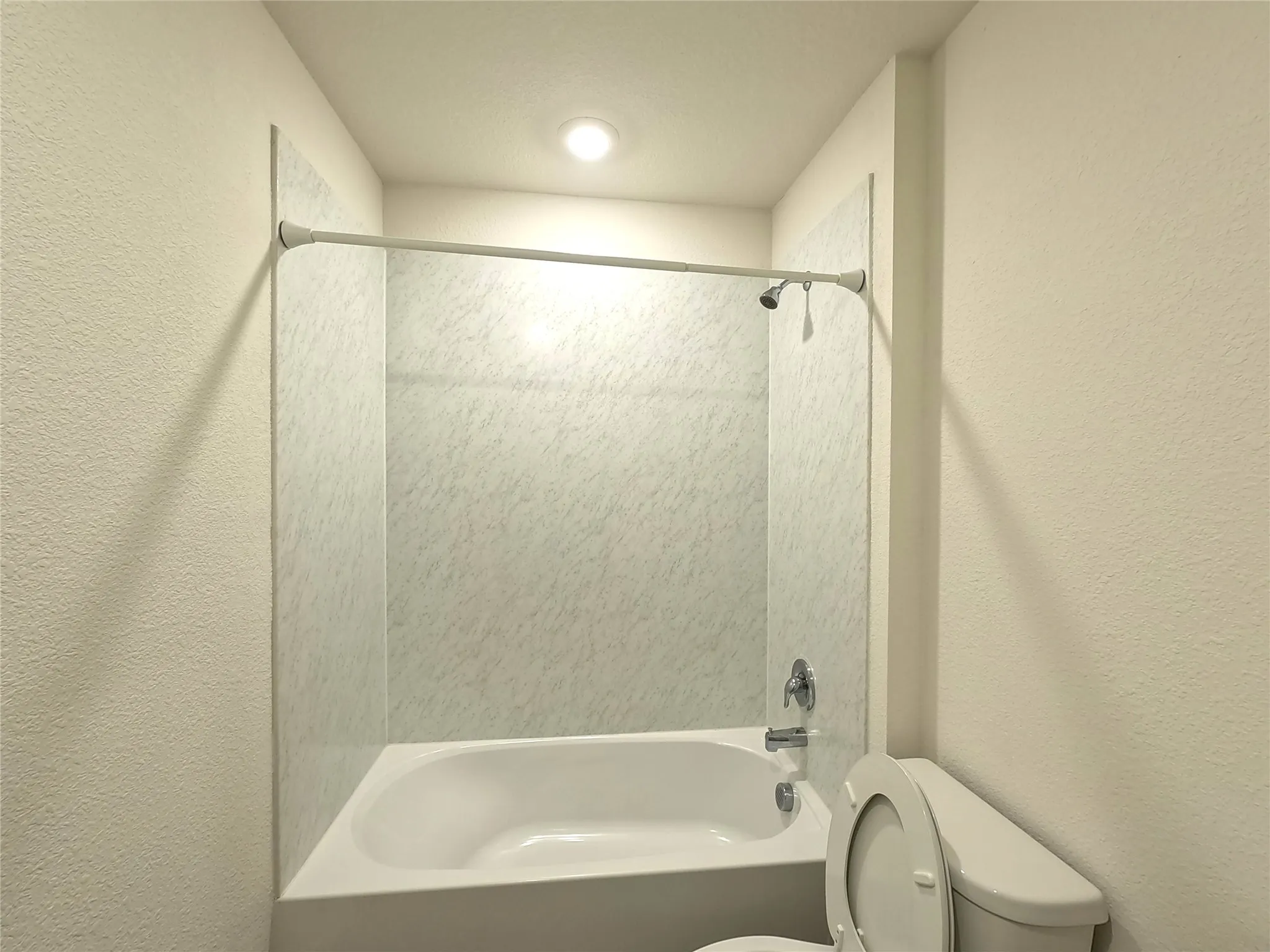 Recessed ceiling lighting, full-sized bathtub, integrated shower, chrome fixtures, and a white toilet