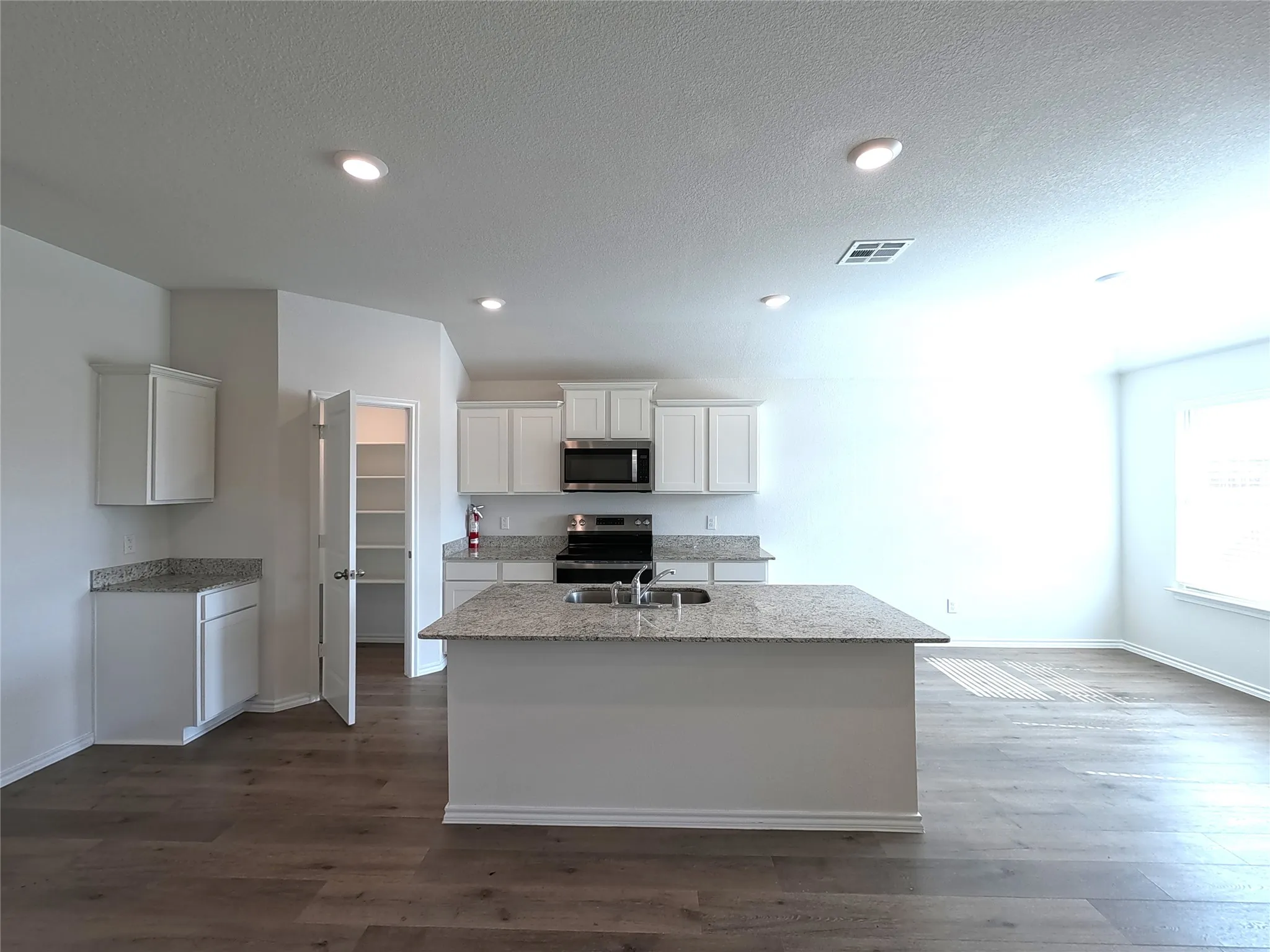 Kitchen featuring an island with a built-in sink, white cabinetry, integrated stainless steel appliances, speckled countertops, and recessed lighting