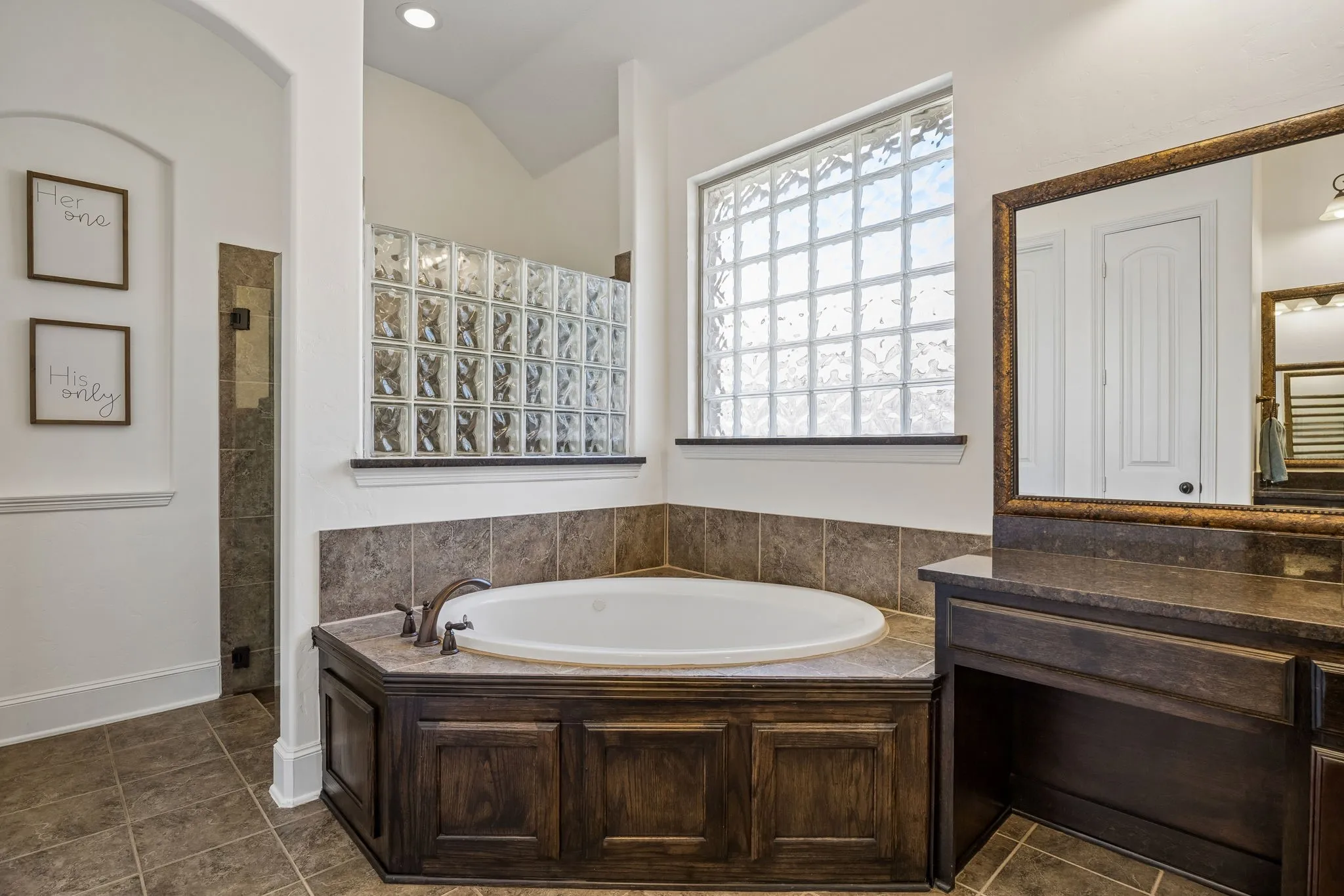 The separate shower is behind the tub with a frameless glass door.