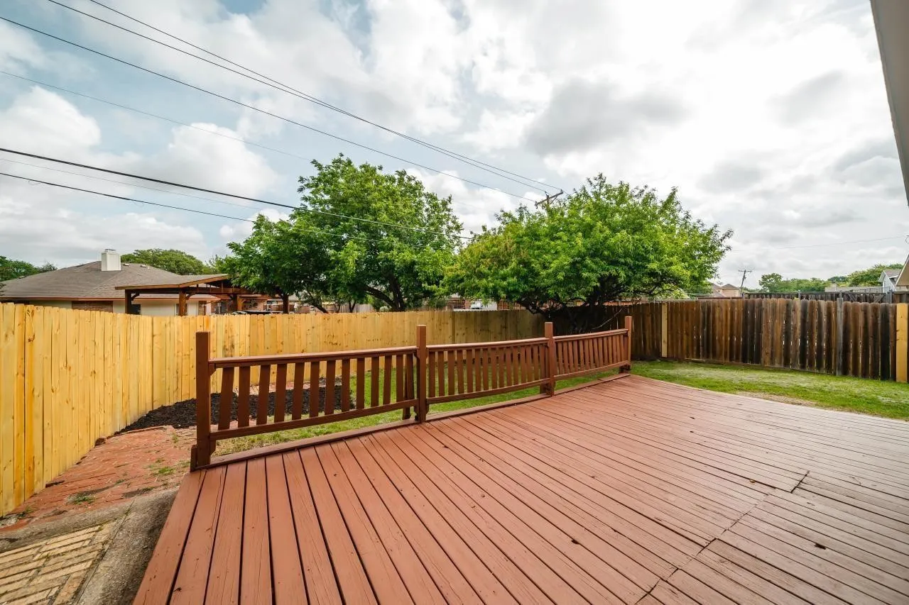 Elevated wooden deck with horizontal railing, enclosed by a full-height wood privacy fence and featuring a brick-paved ground section