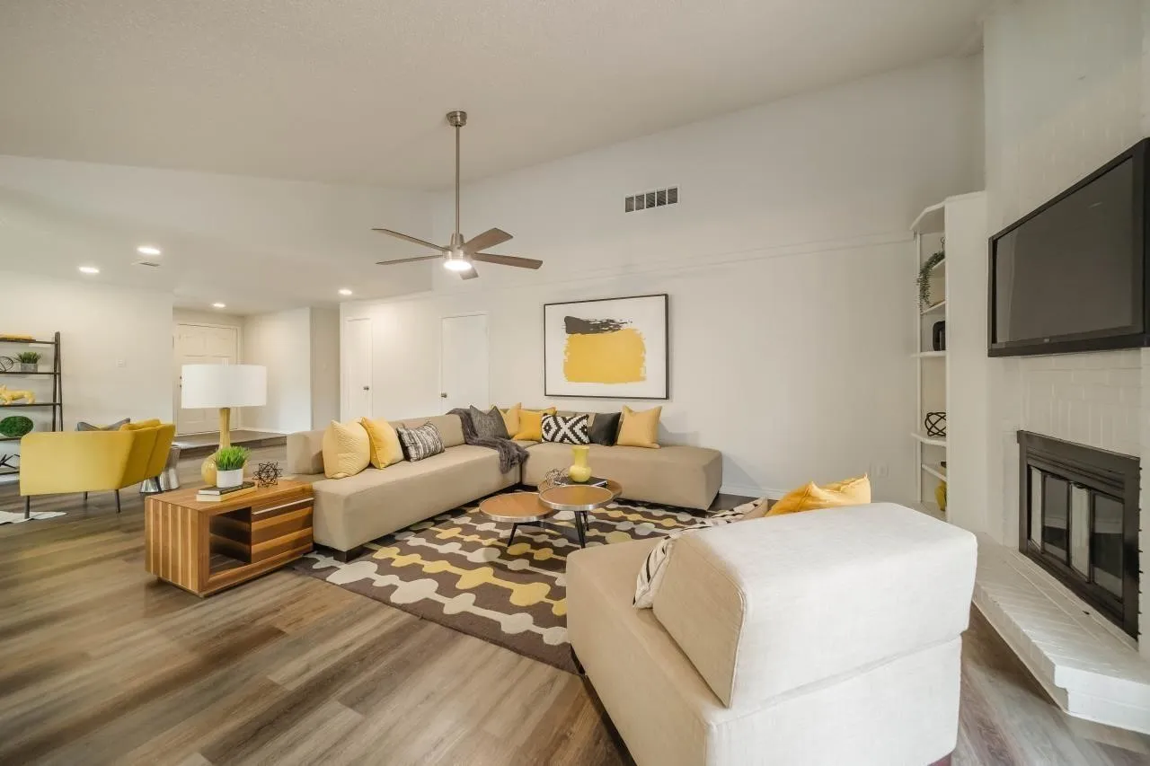 Living area featuring a vaulted ceiling, floor-to-ceiling painted brick fireplace, wood-finish flooring, ceiling fan, and built-in shelving