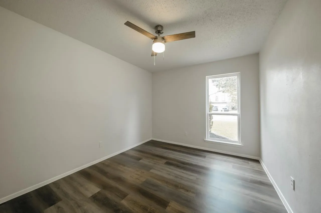 Room featuring wood-finish flooring, a ceiling fan with integrated lighting, and a single-pane window