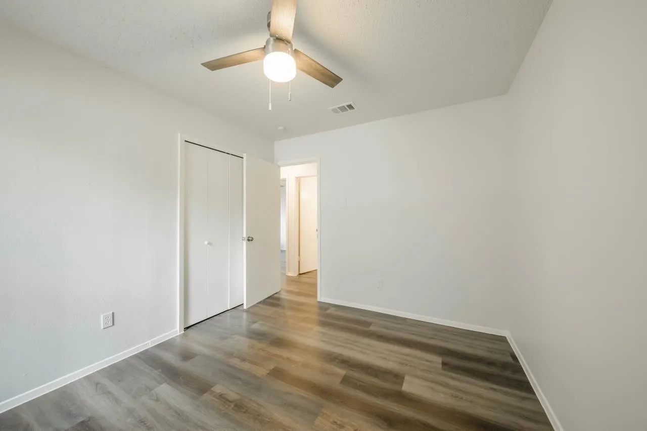 Room featuring wood-finish flooring, a ceiling-mounted light fixture with fan, and a closet with dual folding doors