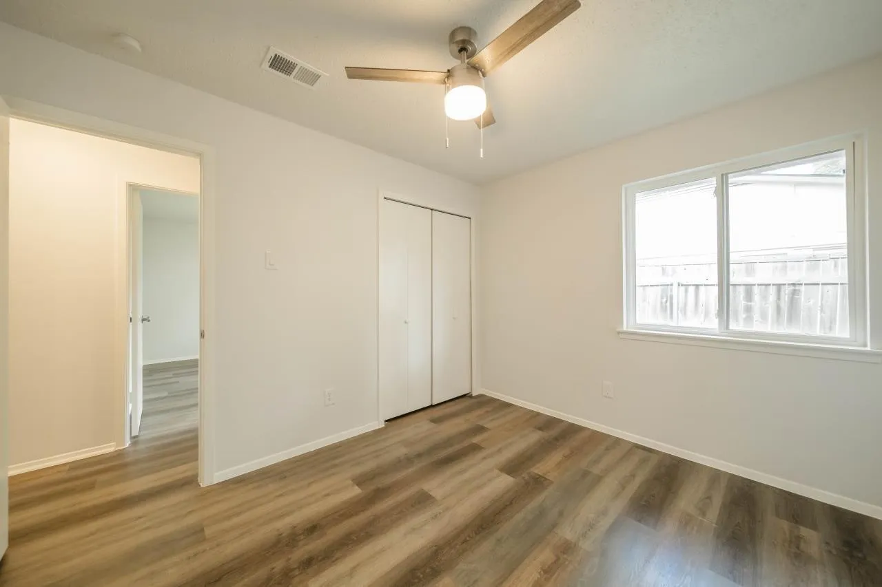 Interior room featuring wood-finish flooring, a ceiling fan with integrated lighting, and a double-door closet