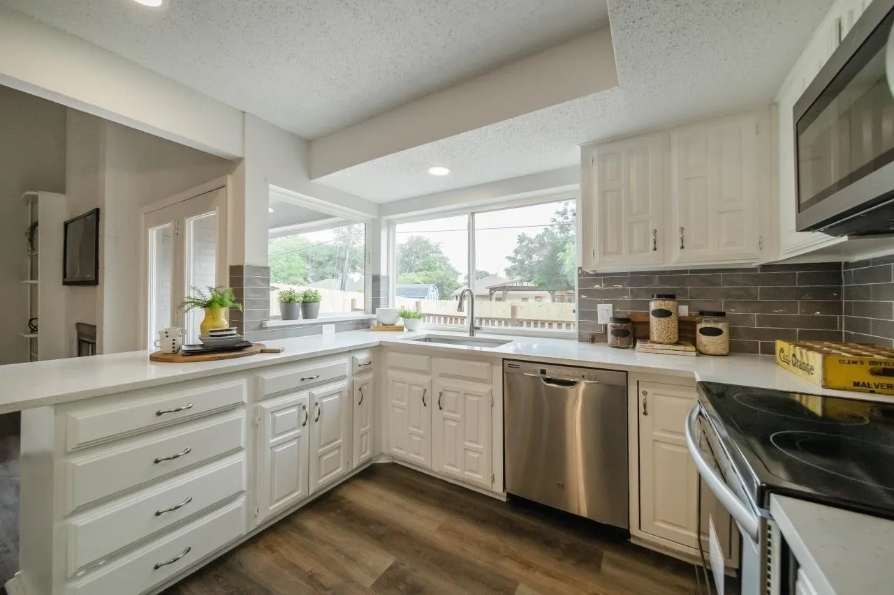 Kitchen featuring white cabinetry, solid-surface countertops, grey subway tile backsplash, stainless steel dishwasher, and wood-finish flooring