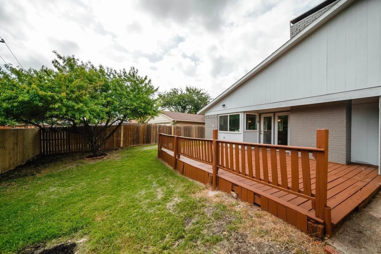 Backyard featuring a raised wood deck, perimeter wood fencing, a mature tree, and a grass lawn