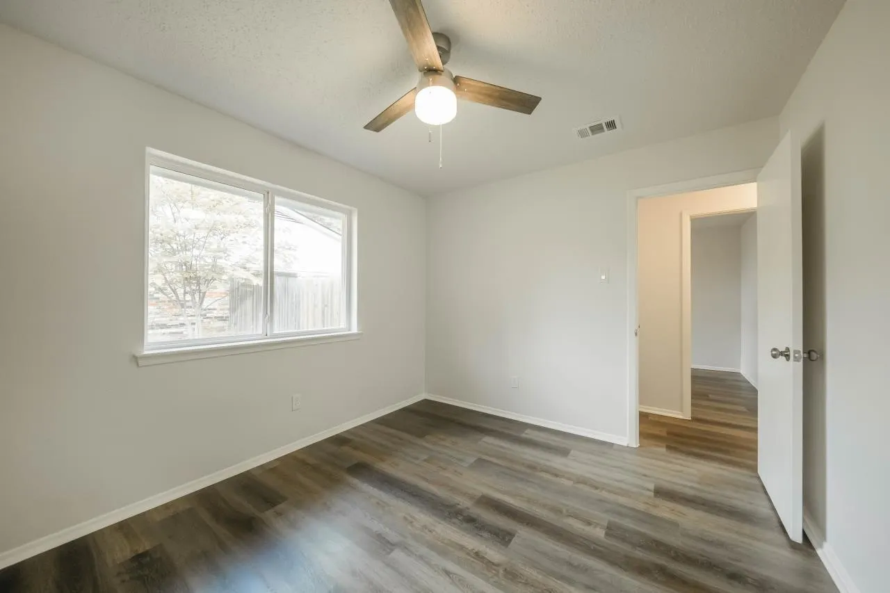 Neutral-toned interior featuring wood-finish flooring, a ceiling fan with integrated lighting, and a large window