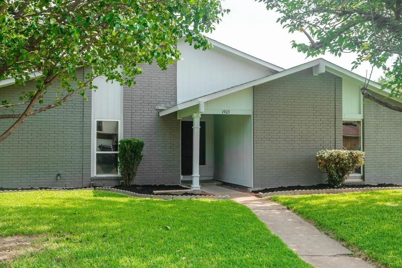 Exterior featuring grey brick facade, vertical wood-panel siding, covered entryway with a column, and a concrete walkway